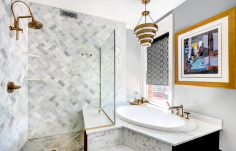 Tiled glass shower and white bathtub in front of a window with a pendant light above.