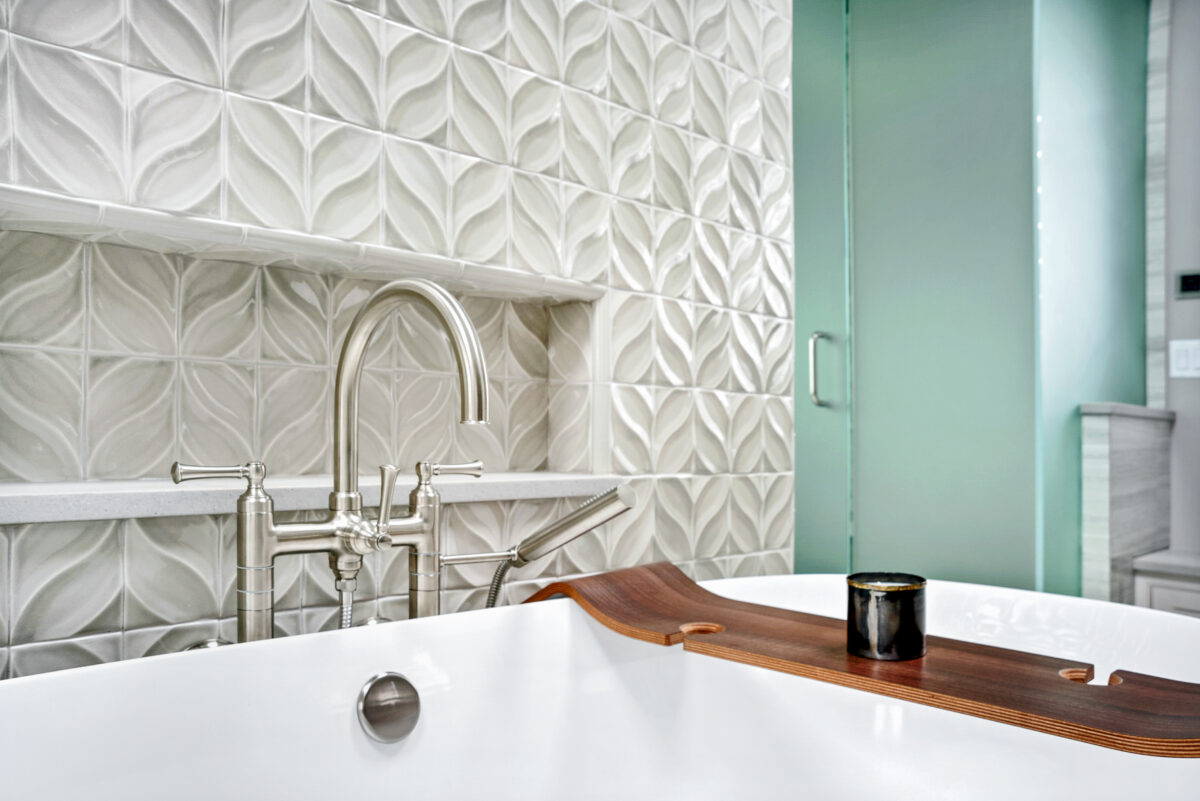 Freestanding tub with nickel finishes in front of decorative wall tile with custom inset shelf.