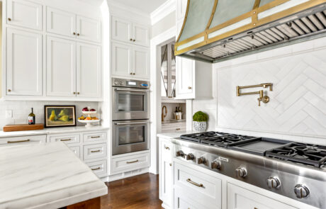 Kitchen renovation with brass range hood and brass wall mounted pot filler faucet.