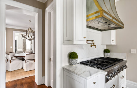 Kitchen renovation with white cabinetry, marble countertops, gas range, and custom brass range hood.