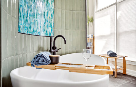 Bathroom Design Inspiration 12 Freestanding white tub with black floor mounted faucet in front of green tiled wall.